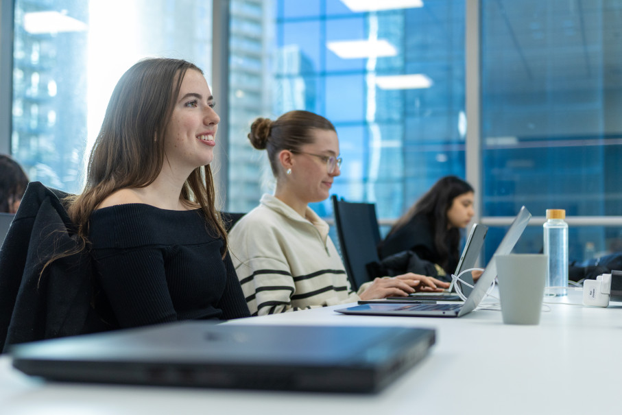 Three women seated at laptops in modern classroom setting