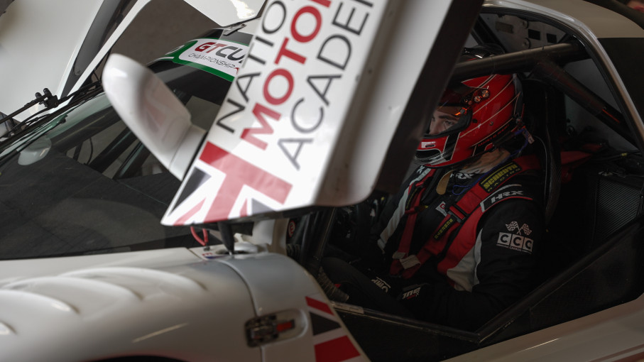 Motor racing driver seated in car wearing helmet