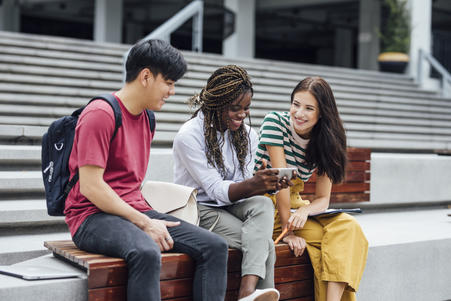 Three students sitting on a bench in a learning environment looking at a mobile phone