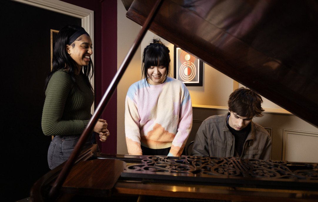 Three pointblank students singing together at a grand piano