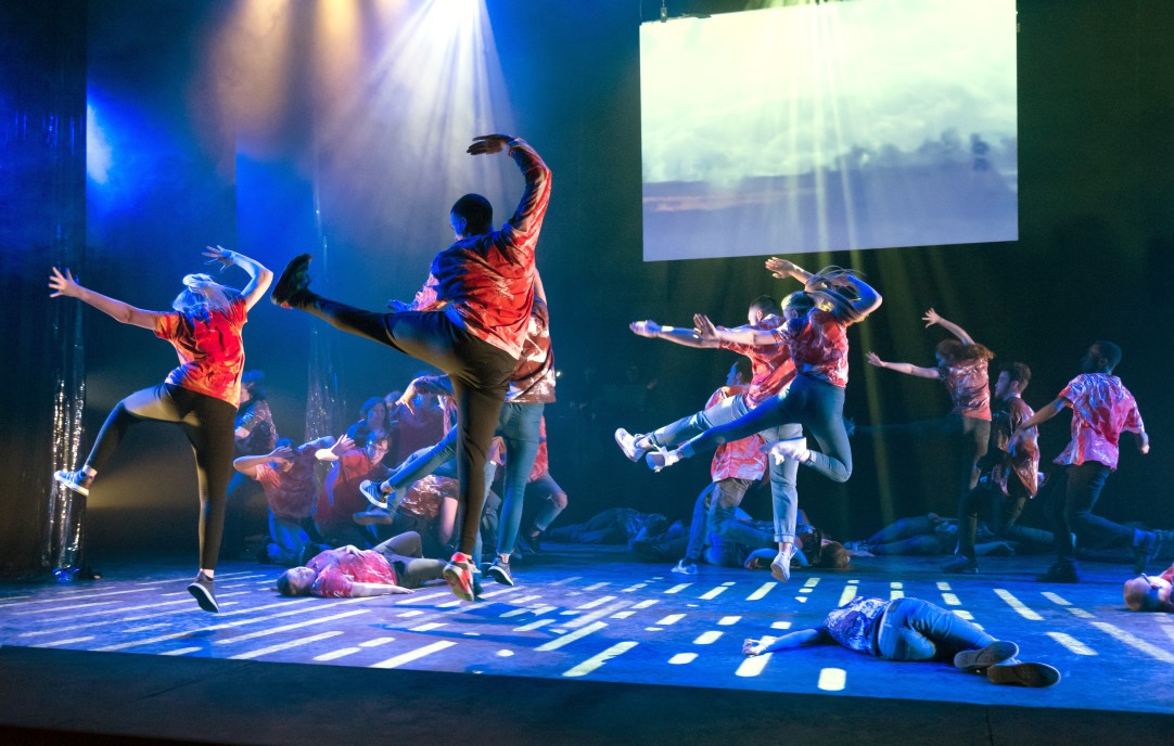 Group of dancers on stage leaping with arms raised