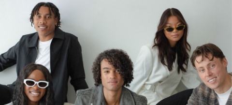 Portrait of five well-dressed Fashion Retail Academy students against a plain wall behind them