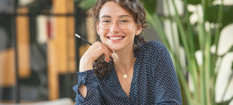 Student sitting at a desk holding a pencil in a modern study environment - she's smiling to camera.