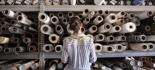 Portrait of textile designer choosing fabric from stack of rolls inside sustainable workshop