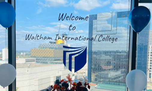 Waltham International College window in a high rise building displaying the words 'Welcome to Waltham International College' with their blue logo beneath as window stickers. Four dark blue and white balloons are around the window corners and flowers below
