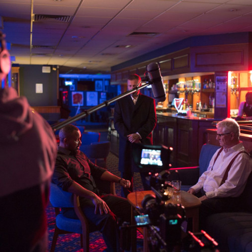 Men being filmed in a pub setting with equipment and microphone