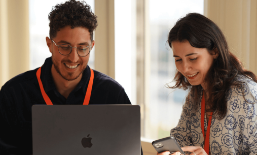 Two people at a desk, one on a laptop, one on a phone