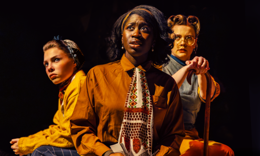 Three women dressed in vintage clothing, acing on stage
