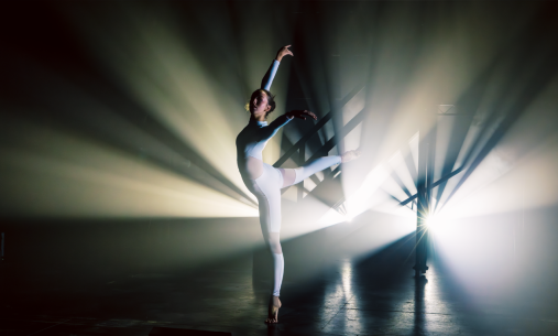 A dancer dressed in all white dancing, backlit by stark white lighting