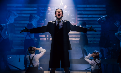 A man beneath a white spotlight, arms wide, singing