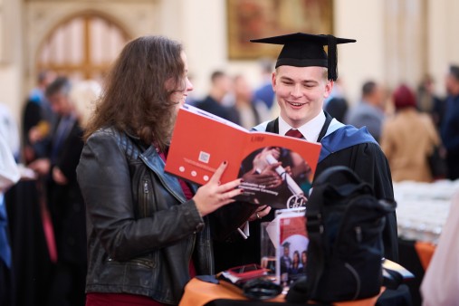 LIBF student wearing graduation attire being shown a brochure by someone