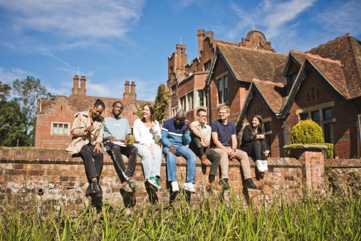A group of Newbold students sitting on a stone wall with the campus building behind them