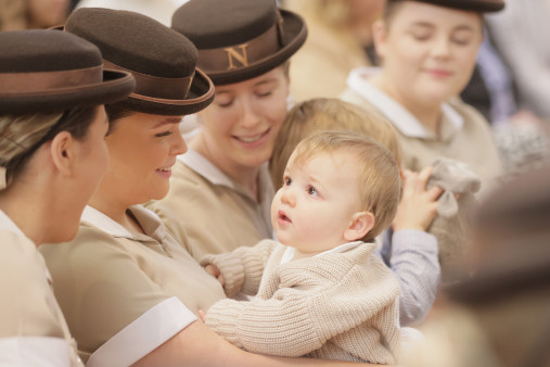Norland nannies in uniform of beige tops and brown hats holding a baby