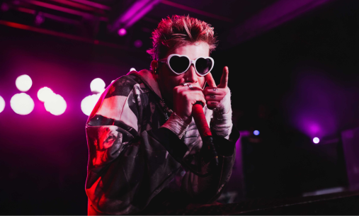 Singer on stage with pink lights and hear shaped sunglasses
