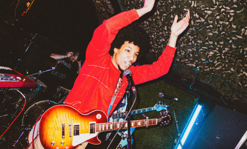 Person on stage wearing guitar and red jumper, clapping